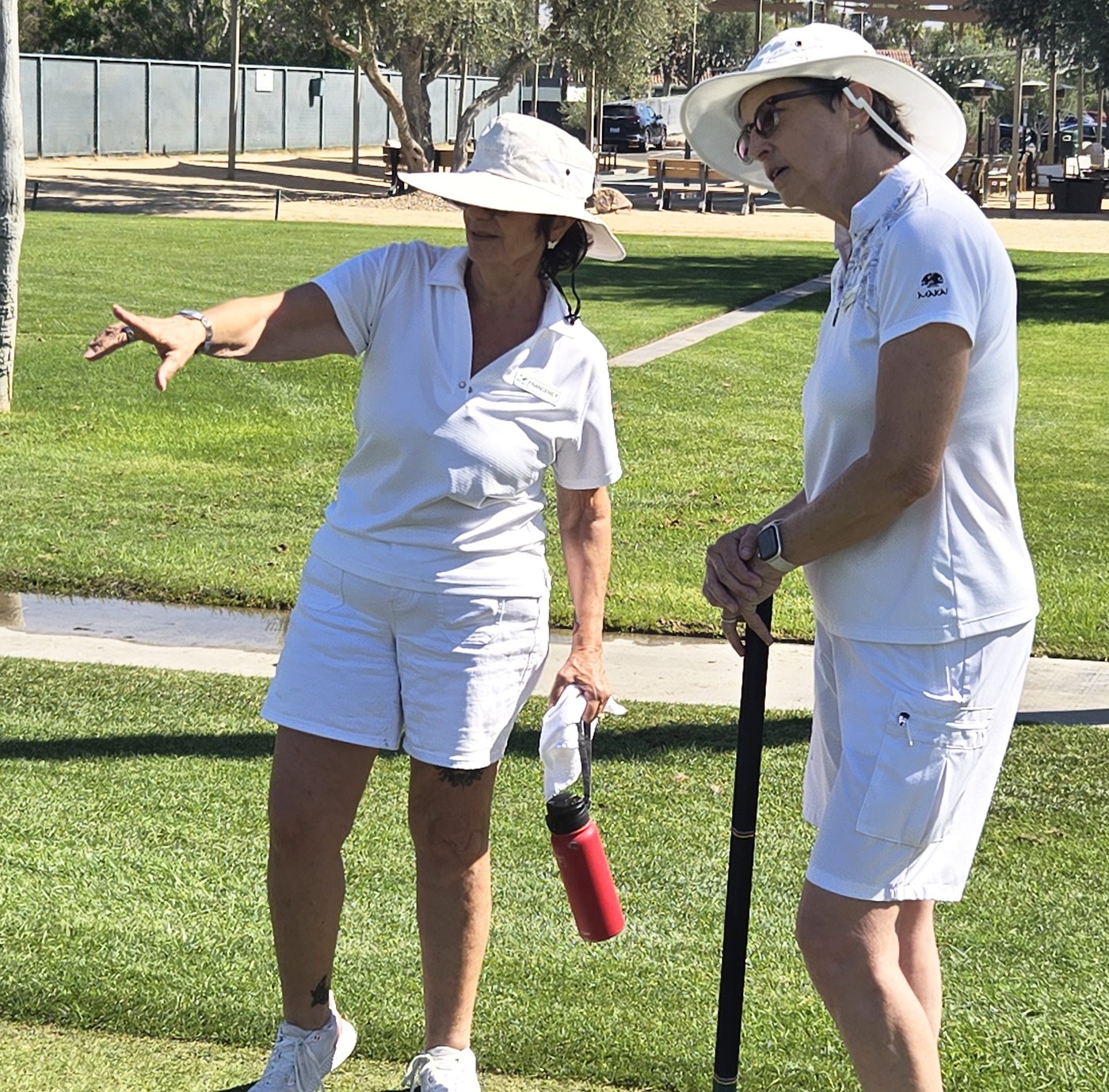 Two members in whites and sun hats discussing the next shot