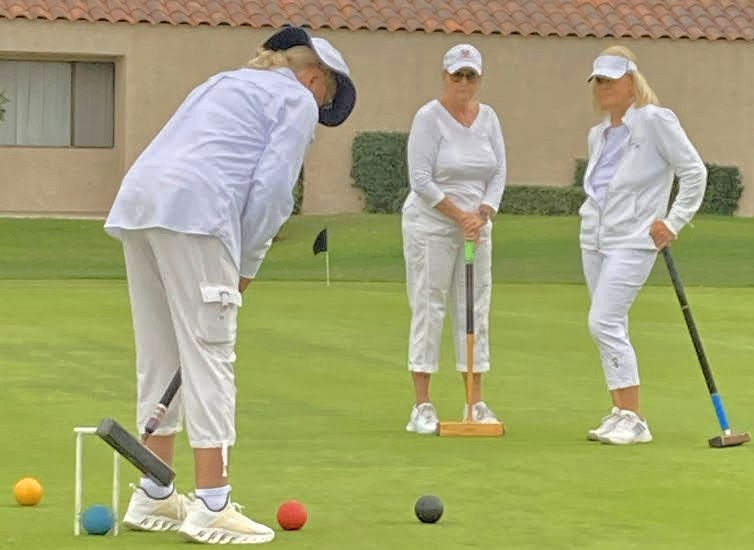 A member taking her shot at the wicket while two players in whites look on